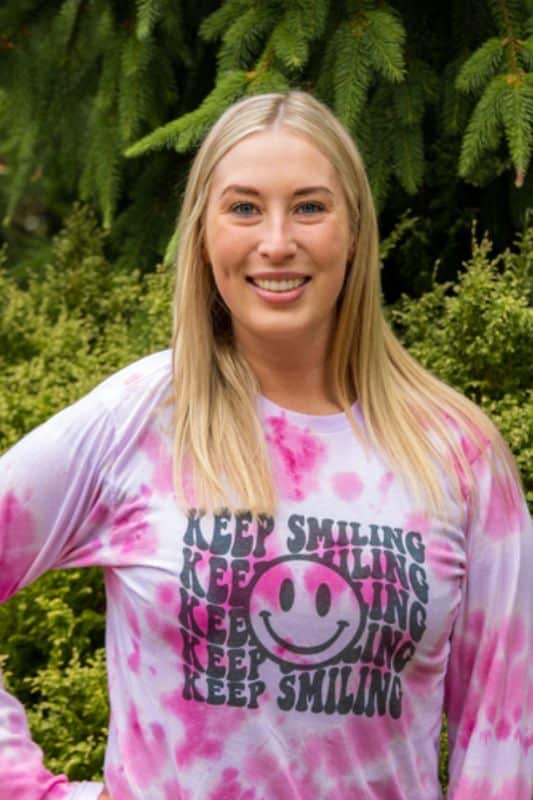 a woman smiling in front of trees