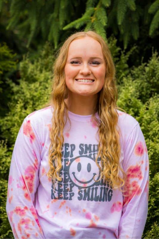 a woman smiling in front of bushes