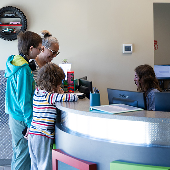 Parent and children at front desk smiling as front desk team helps out the family