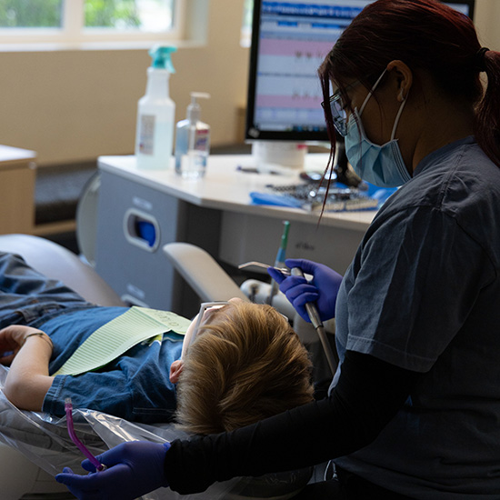 Dental assistant showing child the tool they will use for cleaning