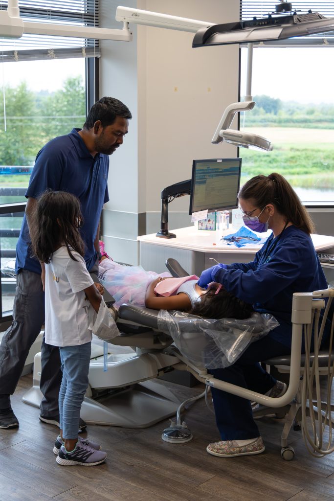 Parent watches dental assistant clean child's teeth